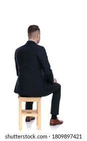 Rear view of a handsome businessman sitting on a chair on white studio background