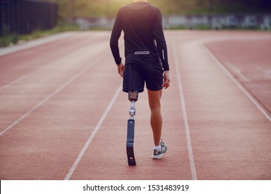 Rear view of handsome caucasian handicapped young man with artificial leg and dressed in shorts and sweatshirt walking on racetrack. - Powered by Shutterstock