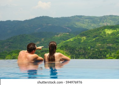 Rear view of happy couple in the pool looking at mountain landscape.
Enjoying beautiful mountains. Man, woman together on summer travel to luxury resort. Summertime relax.