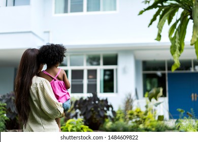 Rear View Of Happy Diverse Family Or Parents Looking At House. Single Mom Standing In Front Of Her Home With Her Little Girls. Multiethnic People With New Care Center. Orphan Care Organization Concept