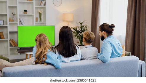 Rear view. Happy family parents and children watching tv sports and entertainment shows on green screen chrome key sitting on sofa in modern apartment. - Powered by Shutterstock