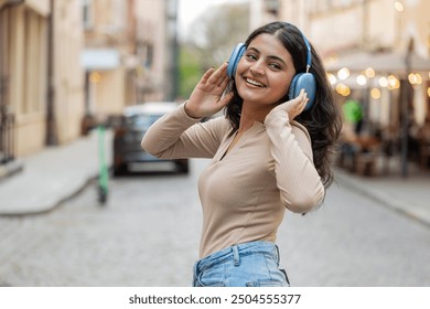 Rear view of happy Indian young woman in wireless headphones dancing listening favorite energetic disco music in smartphone dancing outdoors. Hispanic girl walking on urban city street. Town lifestyle - Powered by Shutterstock