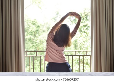 Rear view. Happy, Relaxed Asian woman waking up and stretching her arms on green natural background at her bedroom in the morning. Resting on Holiday. - Shutterstock ID 736607257