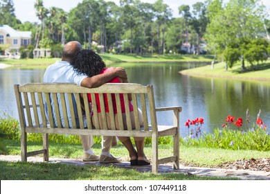 Rear view of a happy romantic senior African American couple sitting on a park bench embracing looking at a lake