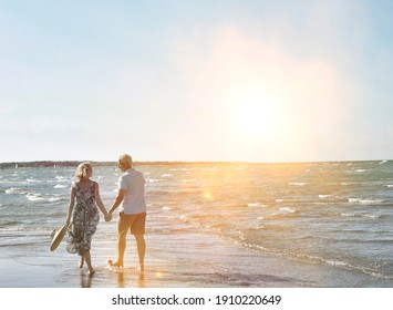 Rückblick auf glückliche ältere Ehepaare, die Händen halten und am tropischen Strand spazieren gehen