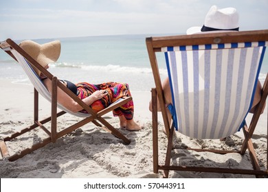 Rear view of happy senior couple relaxing on deckchairs at beach on a sunny day