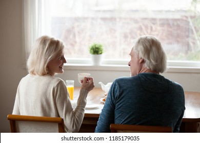 Rear view at happy senior old couple sitting at dining table drinking tea and talking at home, smiling middle aged mature family enjoying coffee and pleasant conversation on weekend morning together - Powered by Shutterstock