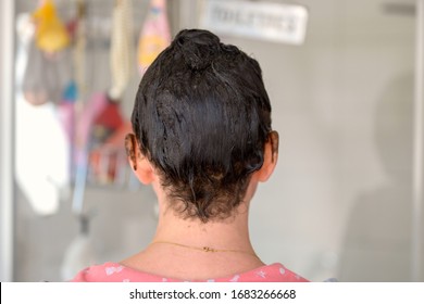 Rear View Of The Head Of A Woman With Hair Dye On Her Hair With Drips On Her Ears As She Waits For The Color To Develop In A Bathroom At Home