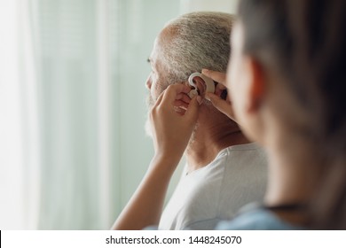 Rear View Of Healthcare Worker Putting Hearing Aid Indoor. Authentic Senior Retired Life Concept