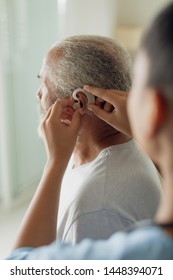 Rear View Of Healthcare Worker Putting Hearing Aid Indoor. Authentic Senior Retired Life Concept