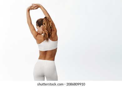 Rear view of healthy fitness woman with strong body, back abs, raising hands up and stretching arms, training in gym, yoga stretch classes, white background