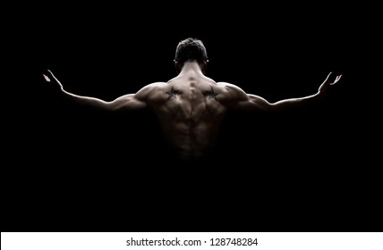Rear view of healthy muscular young man with his arms stretched out isolated on black background - Shutterstock ID 128748284