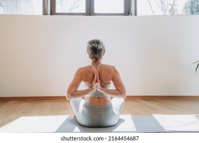 Rear view of healthy women in top bra practicing yoga indoors, sitting with arms behind back doing stretching exercises at home. Yoga and healthy lifestyle concept - Shutterstock ID 2164454687
