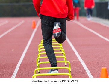 Rear View Of A High School Track Runner Running The Wicket Drill Of Yellow Mini Banana Hurdles In Lane On A Track.