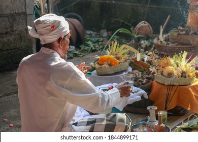 Rear view to Hindu priest praying during a wedding ceremony. Pedanda sits on the ground in front of the offerings and performs wedding ceremonies.