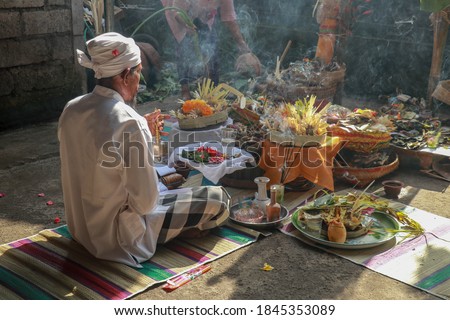 Rear view to Hindu priest praying during a wedding ceremony. Pedanda sits on the ground in front of the offerings and performs wedding ceremonies.