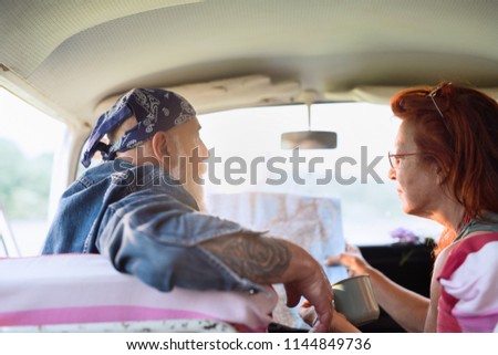Rear view. A hipster senior couple on vacation in a camper van, looking at a road map. the man is tattooed with a white beard and the woman with red hair