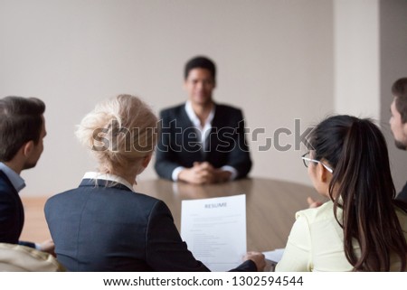 Rear view of hr managers group listen to african male applicant at job interview, recruiters employers talk to seeker making hiring decision meeting vacancy candidate, staffing recruitment concept
