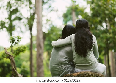 Rear view of hugging female friends sitting in the park