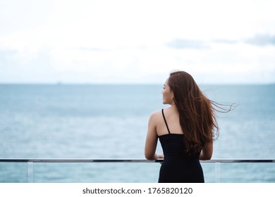 Rear view image of a beautiful young asian woman standing and looking at the sea and blue sky 
