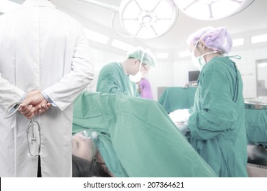 rear view image of doctors with stethoscope in a hospital pose arms crossed behind back looking at nurse pushing stretcher gurney bed in labour room of hospital corridor with female patient pregnant - Powered by Shutterstock