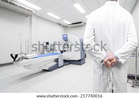  rear view image of doctors with stethoscope pose arms crossed behind back looking at computed tomography or computed axial tomography scan machine in hospital room