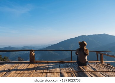 Rear view image of a female traveler sitting on wooden balcony and looking at a beautiful mountain view - Powered by Shutterstock