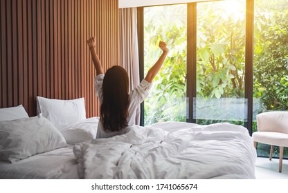 Rear View Image Of A Woman Do Stretching After Waking Up In The Morning  , Looking At A Beautiful Nature View Outside Bedroom Window 