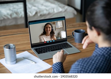 Rear view Indian businesswoman chatting with colleague, using laptop, sitting at work desk, smiling female wearing headphones on screen, employees students briefing, brainstorming, chatting online