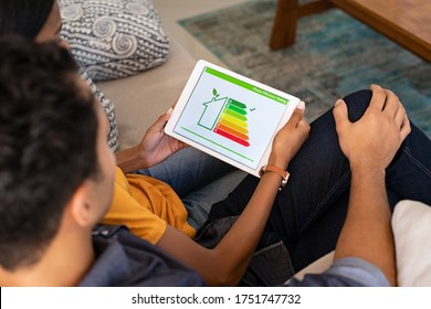 Rear view of indian couple checking on digital tablet housing energy efficiency rate. Husband embracing wife while checking the energy efficiency status of home. Young couple using digital tablet. - Powered by Shutterstock