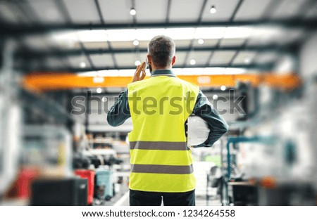 A rear view of an industrial man engineer with smartphone in a factory, working.