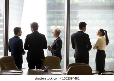 Rear View Of International Executives Team Talking Near Office Window, Multi Ethnic Diverse Business People Silhouette Stand Back Discuss Plans, Corporate Group Racial Discrimination At Work Concept