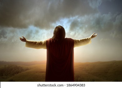Rear view of Jesus Christ raised hands and praying to god with a sunrise sky background