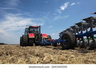 Rear view of a large tractor work with a plow in a field. Start tillage after harvest. Work of agricultural equipment.
