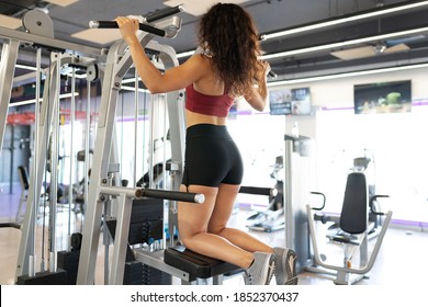 Rear View Of A Latin Young Woman Kneeling And Working Out In A Gym Pull Up Machine 