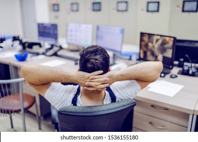 Rear View Of Lazy Factory Worker Sitting On Chair With Hands Behind Head And Sleeping In Control Room.