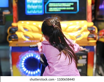 Rear view of little Asian kid girl playing arcade video game. Motorcycle Racing.