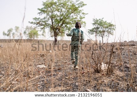 Rear view of a little black African boy walking in the midst of scrub in a dry cornfield in the Sahel region; climate change concept