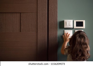 Rear view at little careless child girl exploring house playing turning light switches, home electricity danger security, electric shock risk and kids safety, energy power saving concept, copy space