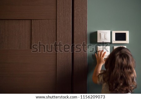Rear view at little careless child girl exploring house playing turning light switches, home electricity danger security, electric shock risk and kids safety, energy power saving concept, copy space