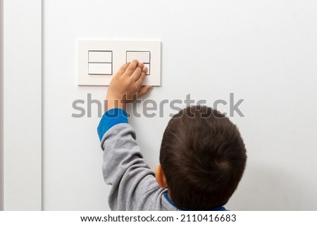 Rear view at little careless child boy exploring house playing turning light switches, home electricity danger security, electric shock risk and kids safety, energy power saving concept, copy space