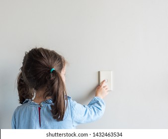 Rear view of little girl turning off Australian light switch on neutral wall background with copy space (selective focus)