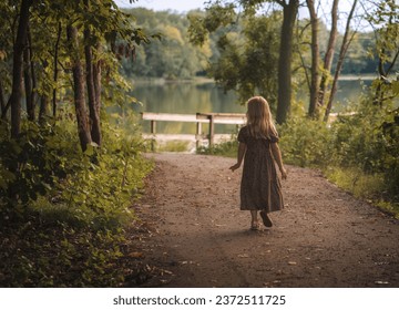 A rear view of a little girl walking in the autumn park by the lake