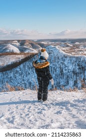 Rear View Of A Little Girl In Warm Clothes Standing On A Mountain With A Beautiful Winter Snowy Landscape