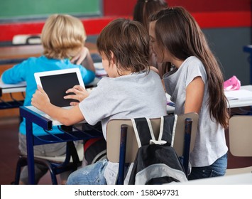 Rear view of little schoolchildren using digital tablet at desk in classroom