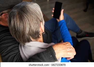 Rear View Of Loving Senior Couple At Home Making Video Call To Family On Mobile Phone