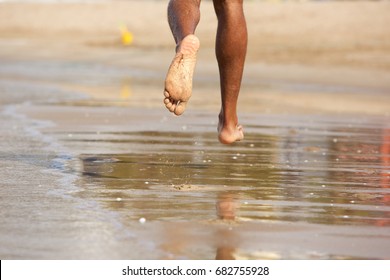 Rear View Low Angle View Of Man Running Barefoot Along Beach