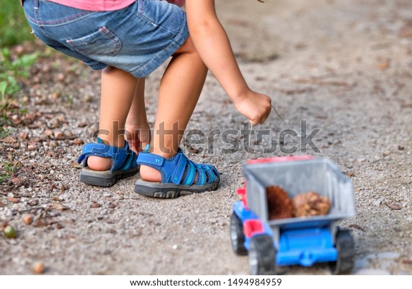Rear view of the lower section of a 3-4 year old\
child in short trousers in summer picking up something from the\
ground to put it into a toy\
truck