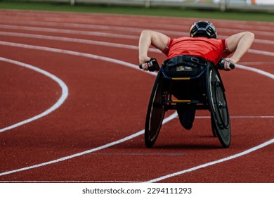 rear view male athlete in racing wheelchair riding on red track stadium, summer para athletics championships - Powered by Shutterstock