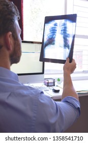 Rear View Of Male Caucasian Doctor Looking At X Ray In Clinic 